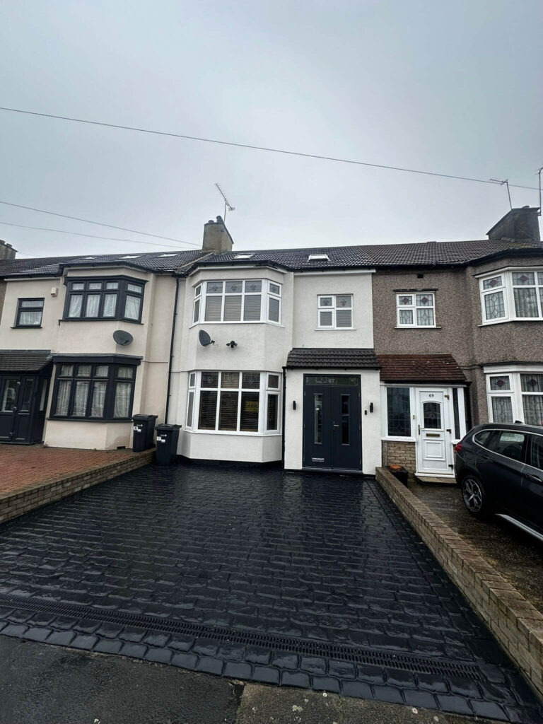 House front with white walls, white bay windows, a dark entrance door and a black paved driveway.