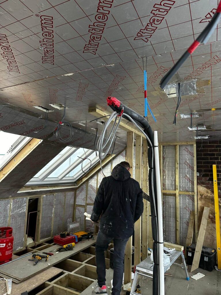 Loft room during construction with insulation boards, exposed timber framing, services and roof windows.