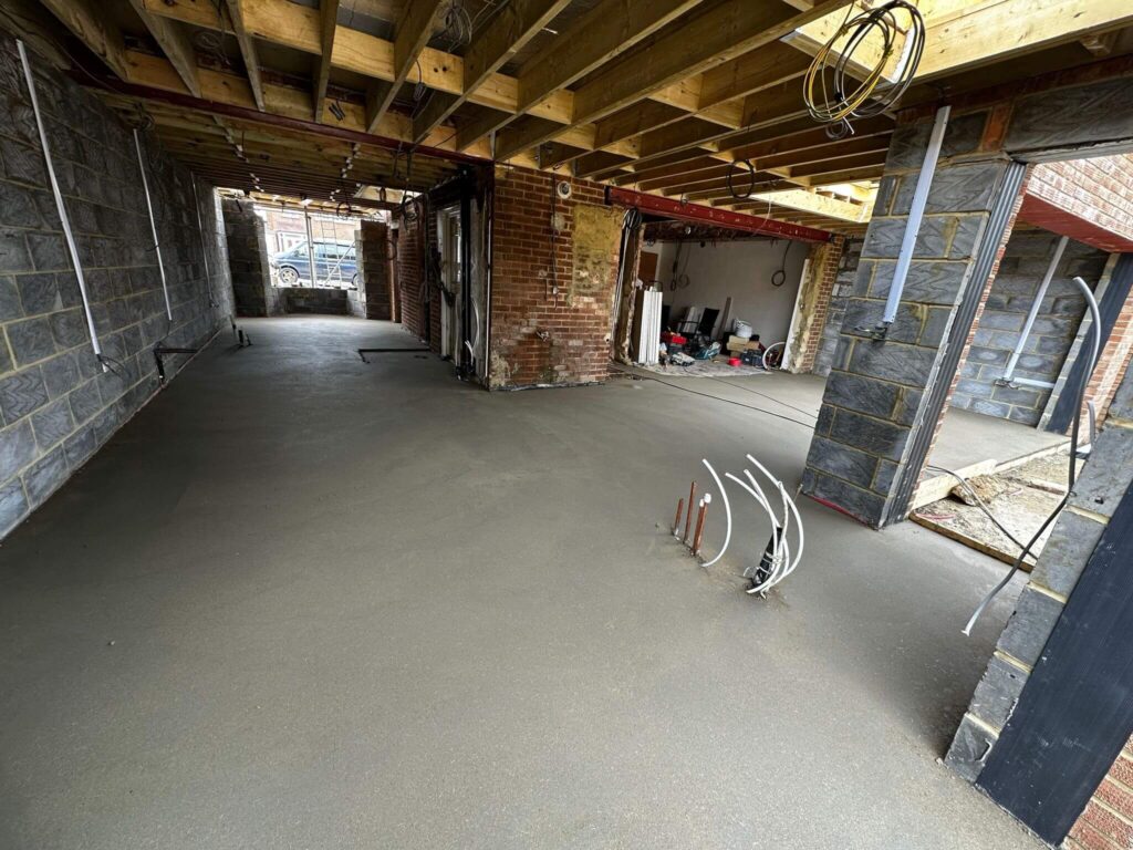 Interior during construction with exposed ceiling joists, blockwork, steel beams, services and a bare floor.