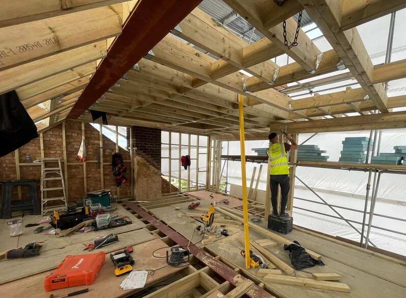 Loft construction with exposed timber joists, steel beams, wall framing and scaffold weather protection.