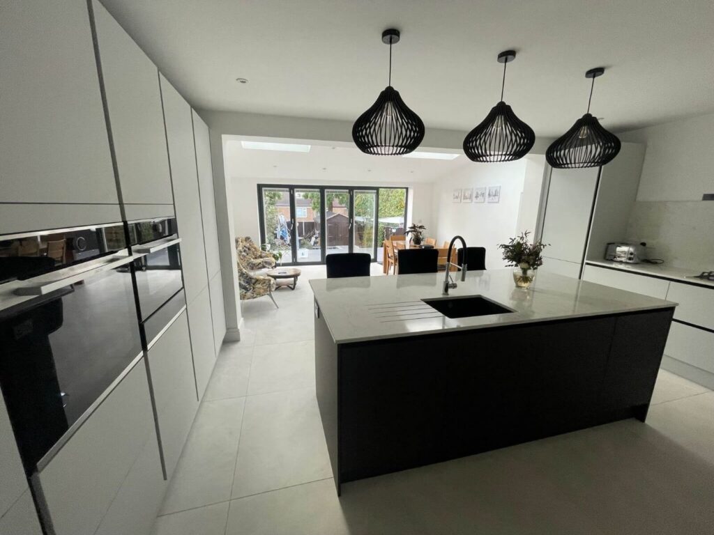 Open-plan kitchen with white cabinets, a dark island, three pendant lights and glazed garden doors.