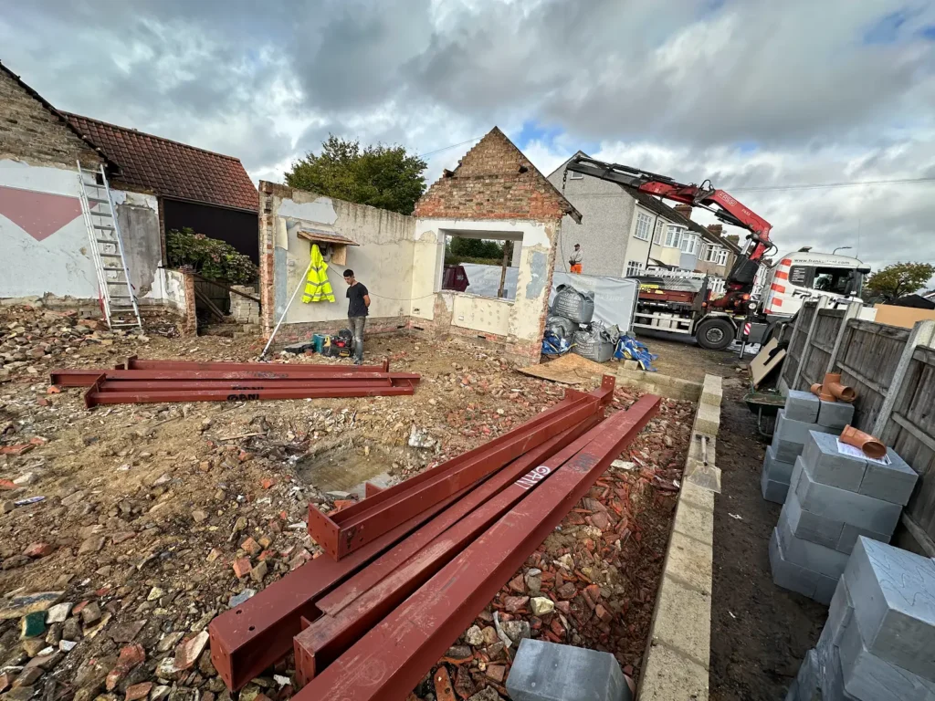 Red steel beams beside exposed walls, with a delivery crane at the Hornchurch site