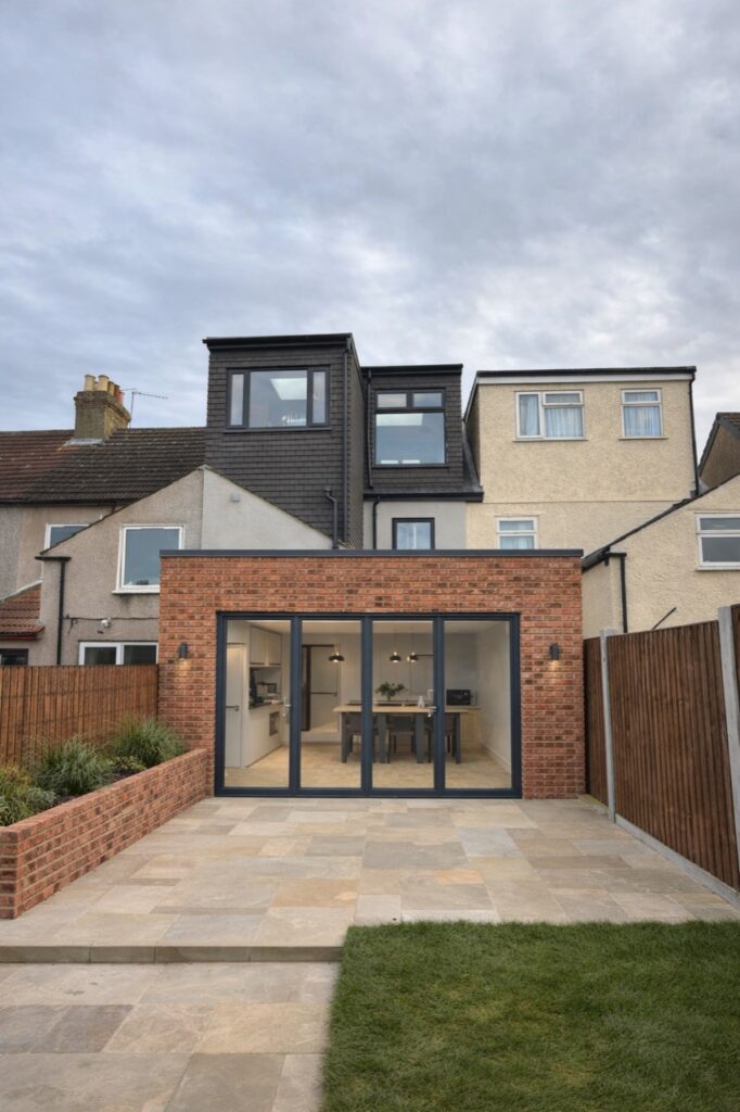 Completed brick rear extension with glazed doors, patio and dormer windows above
