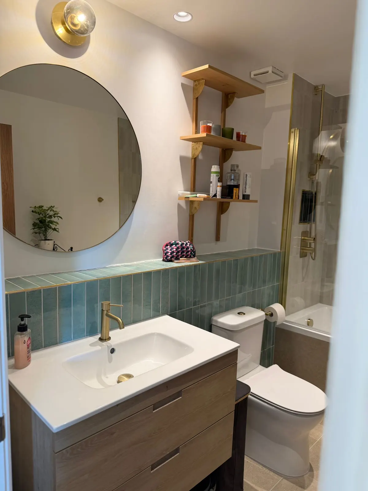 Bathroom vanity beneath a round mirror, with blue-green tiles and gold-toned fittings