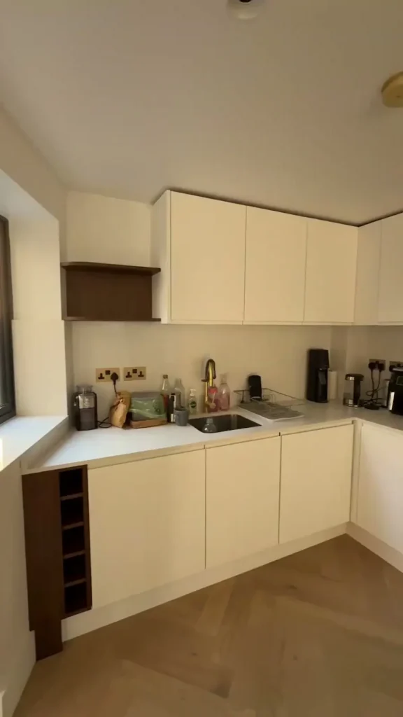 Light kitchen cabinetry, inset sink and gold-toned tap above herringbone-pattern flooring