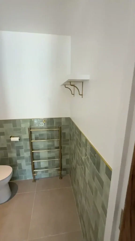 Blue-green bathroom wall tiles with a gold-toned towel rail and matching trim
